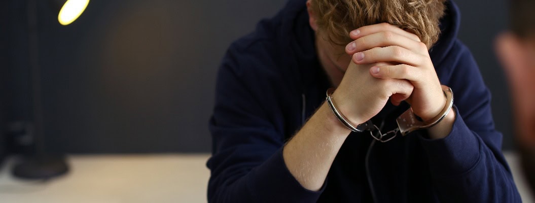 Mann in Handschellen an einem Schreibtisch in einem Gebäude festgehalten, Platz für Text. Strafrecht
