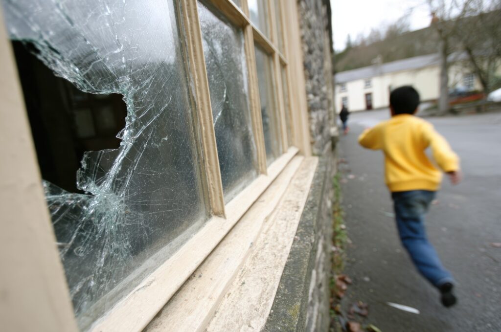 Ein Junge rennt die Straße hinunter, nachdem er mit einem Stein eine Fensterscheibe zerschlagen hat